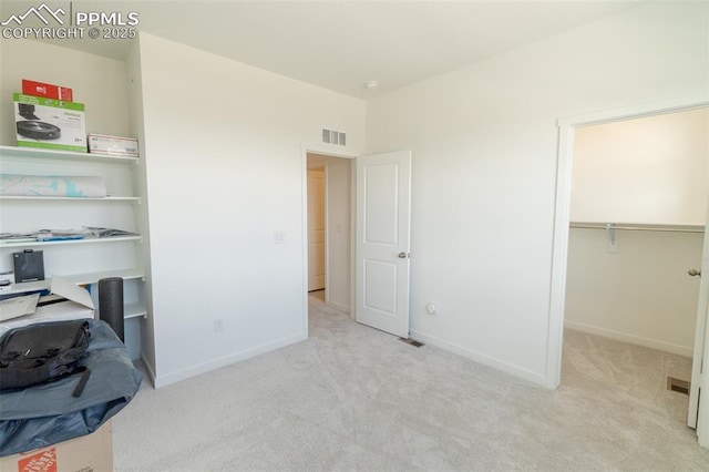 unfurnished bedroom with a walk in closet, carpet floors, visible vents, and baseboards