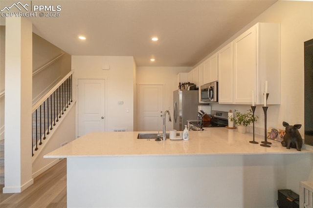 kitchen with white cabinetry, light wood-style flooring, a peninsula, appliances with stainless steel finishes, and recessed lighting