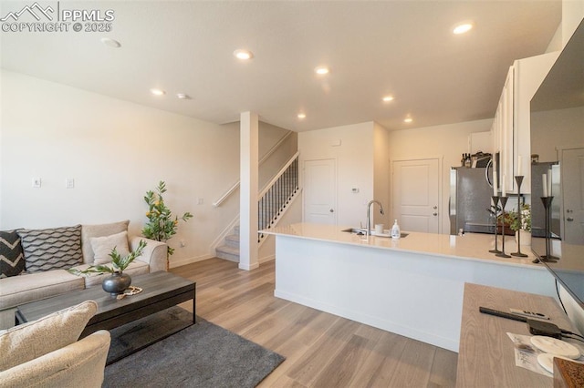 kitchen with a sink, freestanding refrigerator, light wood-style floors, a peninsula, and white cabinetry