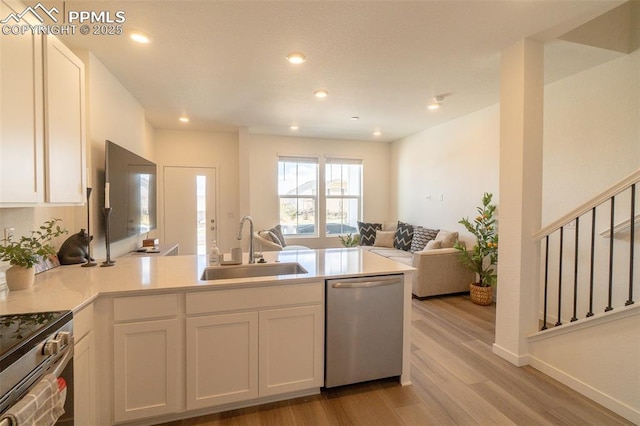 kitchen featuring white cabinets, a sink, a peninsula, light wood-style flooring, and appliances with stainless steel finishes