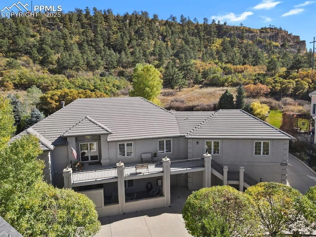 back of property with stucco siding, a tile roof, and a wooded view