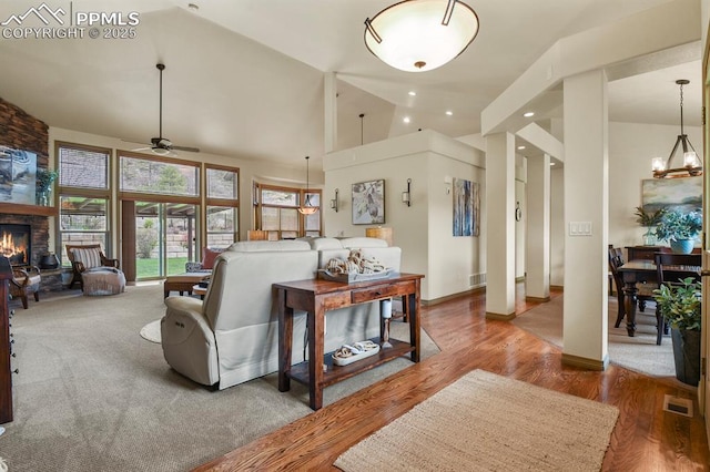 living room featuring ceiling fan, a stone fireplace, visible vents, wood finished floors, and high vaulted ceiling