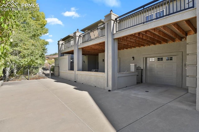 rear view of house with concrete driveway, an attached garage, fence, and stucco siding