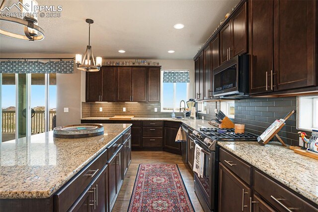 12857 Morning Breeze Way, Peyton, CO 80831 - kitchen with light stone countertops, a sink, a center island, stainless steel microwave, and gas range