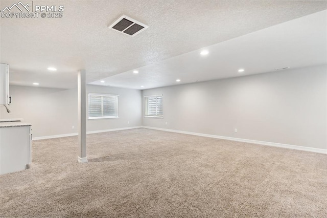 below grade area with a textured ceiling, visible vents, baseboards, recessed lighting, and light carpet