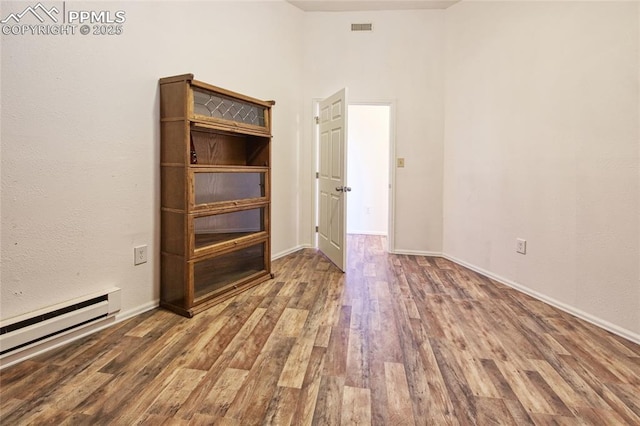 unfurnished room with baseboards, wood finished floors, visible vents, and baseboard heating