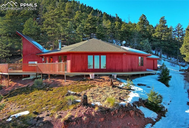 exterior space featuring a wooden deck, a view of trees, and roof with shingles
