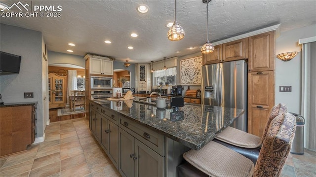 17770 Radbourne Ct, Monument, CO 80132 - kitchen with stainless steel appliances, arched walkways, recessed lighting, a large island with sink, and a breakfast bar area