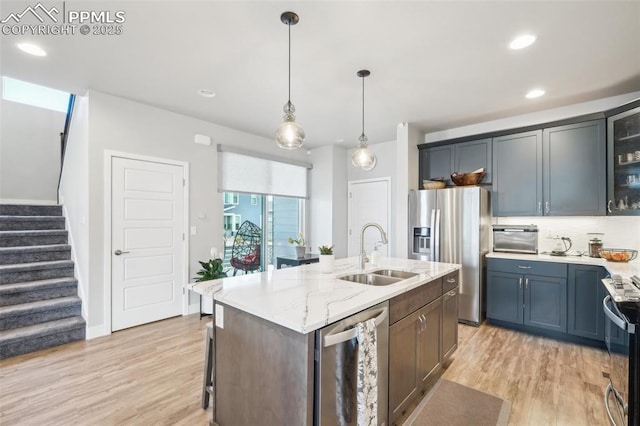 kitchen featuring stainless steel appliances, an island with sink, a sink, and light wood-style flooring