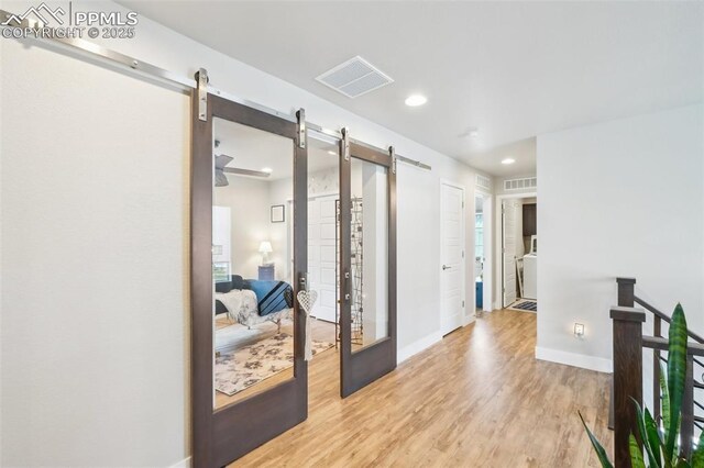 corridor with visible vents, baseboards, recessed lighting, a barn door, and light wood finished floors
