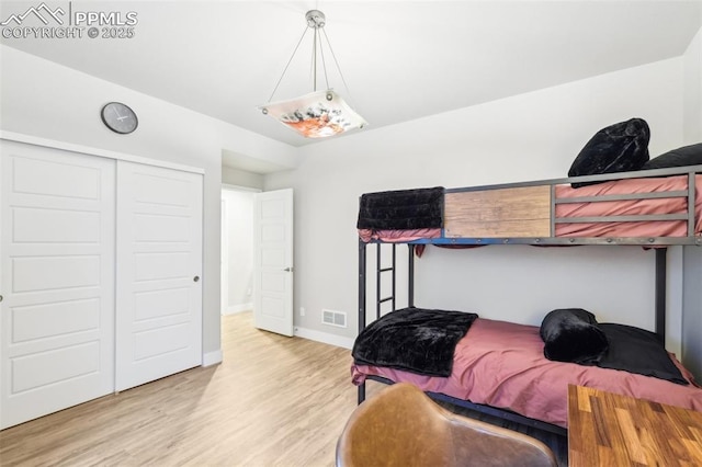 bedroom with baseboards, visible vents, wood finished floors, and a closet