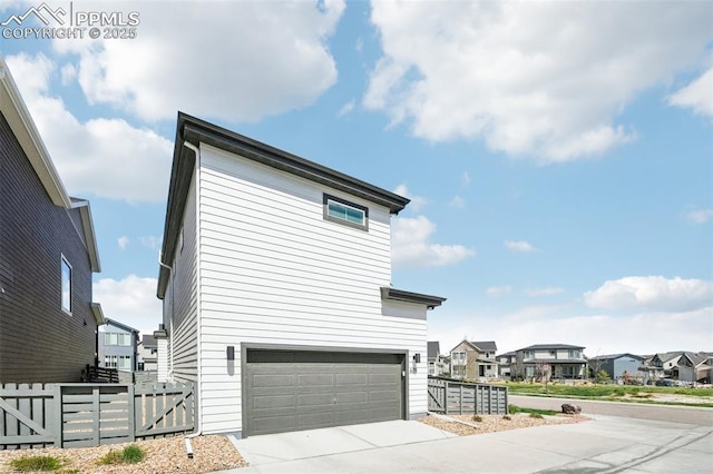 view of home's exterior with fence, an attached garage, driveway, and a residential view