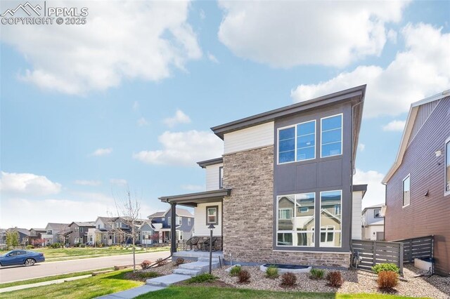 contemporary home featuring a residential view, fence, stone siding, a porch, and a front yard