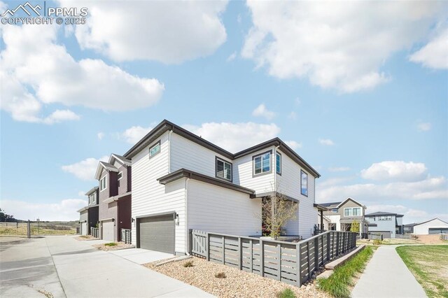 view of side of home with fence, an attached garage, concrete driveway, and a residential view