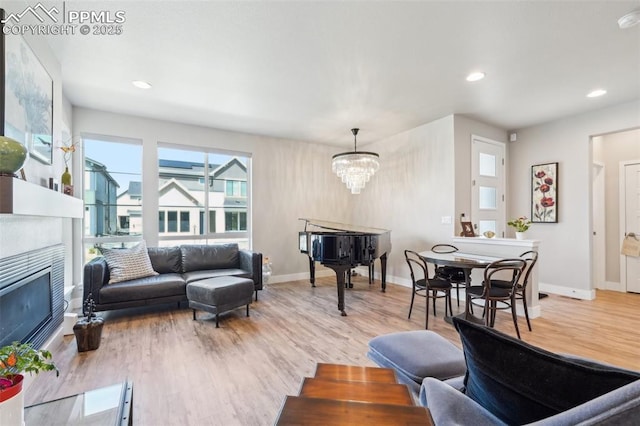 living room with a notable chandelier, a fireplace, recessed lighting, baseboards, and light wood-type flooring