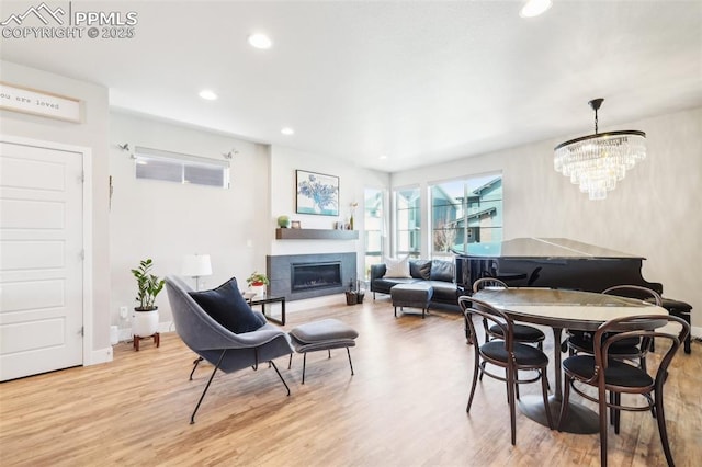 dining room with wood finished floors, baseboards, a notable chandelier, a glass covered fireplace, and recessed lighting
