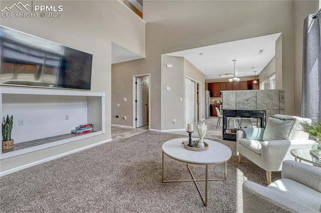 living room featuring a towering ceiling, a fireplace, baseboards, light colored carpet, and a notable chandelier