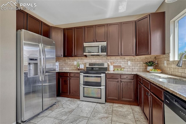 kitchen featuring stainless steel appliances, light stone countertops, a sink, and tasteful backsplash