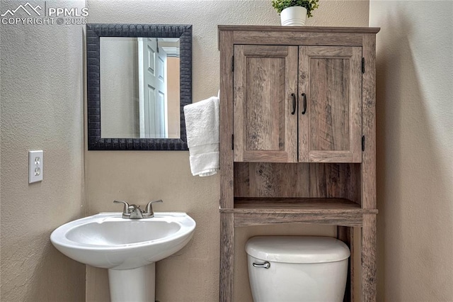 bathroom featuring a sink, a textured wall, and toilet