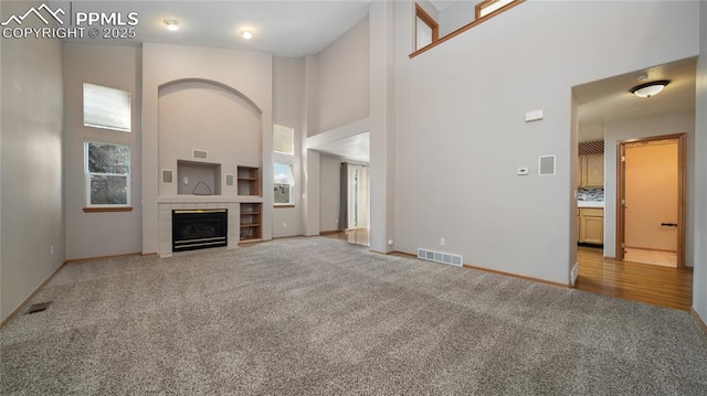 unfurnished living room featuring light colored carpet, a towering ceiling, baseboards, and a tile fireplace
