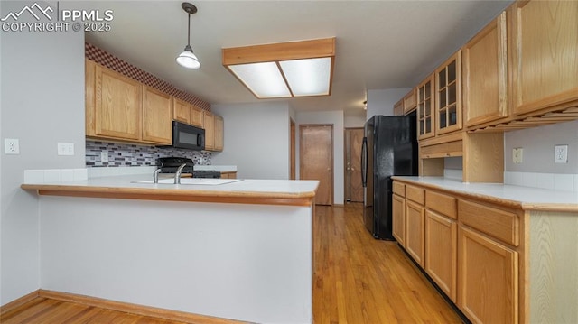 kitchen with black appliances, a peninsula, glass insert cabinets, light wood-type flooring, and decorative backsplash