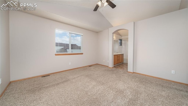 unfurnished bedroom featuring light colored carpet, baseboards, arched walkways, lofted ceiling, and ensuite bath