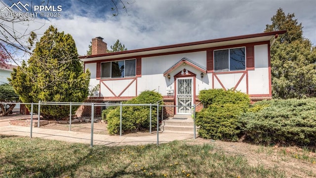 view of front of house featuring fence, a chimney, and brick siding
