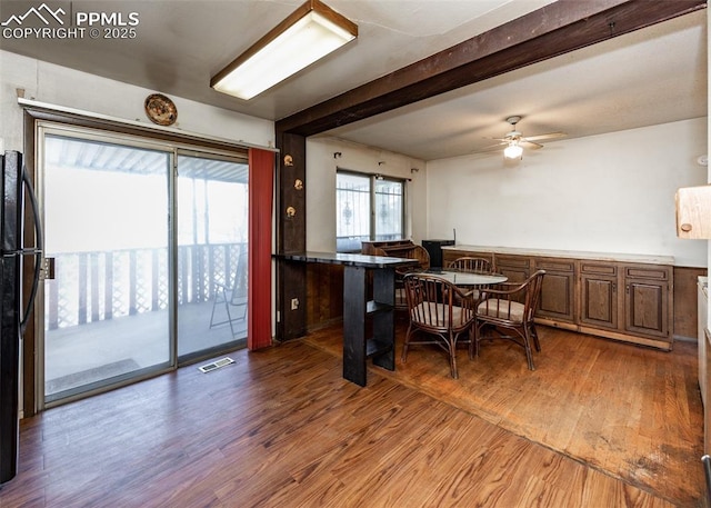 dining space with wood finished floors, visible vents, a ceiling fan, and beamed ceiling