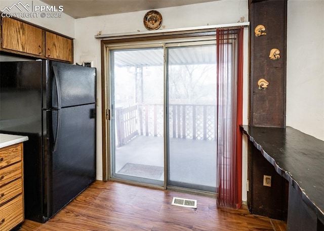 kitchen with dark wood finished floors, visible vents, brown cabinetry, and freestanding refrigerator
