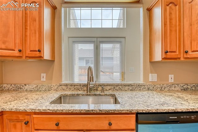 kitchen with dishwashing machine, a sink, brown cabinets, and light stone counters