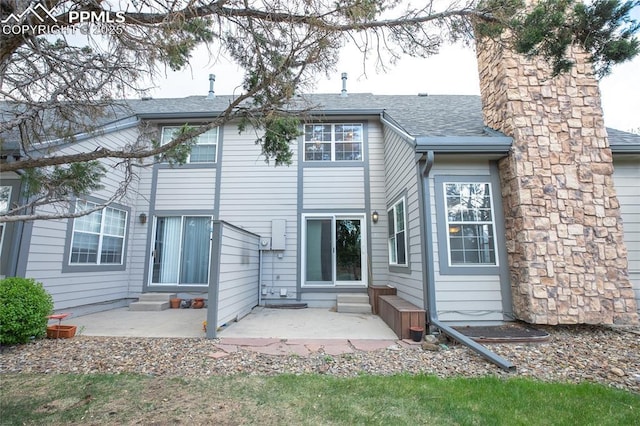 rear view of property with a patio area, entry steps, roof with shingles, and a chimney