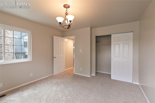 unfurnished bedroom with carpet flooring, a chandelier, a closet, and baseboards