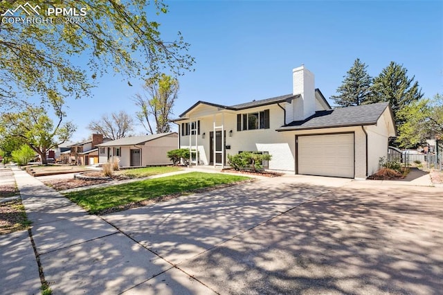 split foyer home featuring a chimney, fence, a garage, concrete driveway, and a front yard