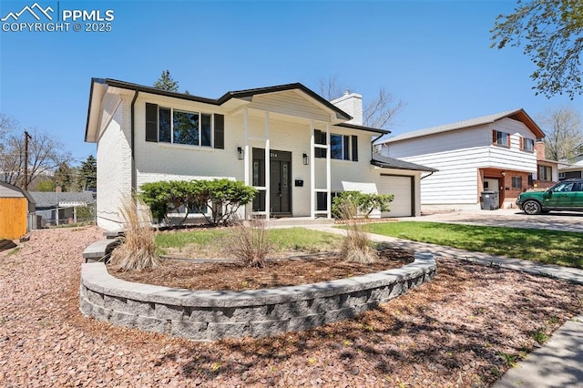 bi-level home featuring brick siding, an attached garage, a chimney, and driveway