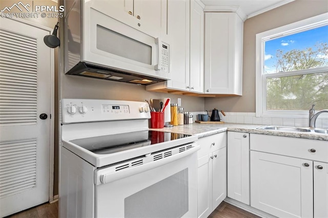 kitchen featuring dark wood-style floors, a sink, crown molding, white cabinetry, and white appliances