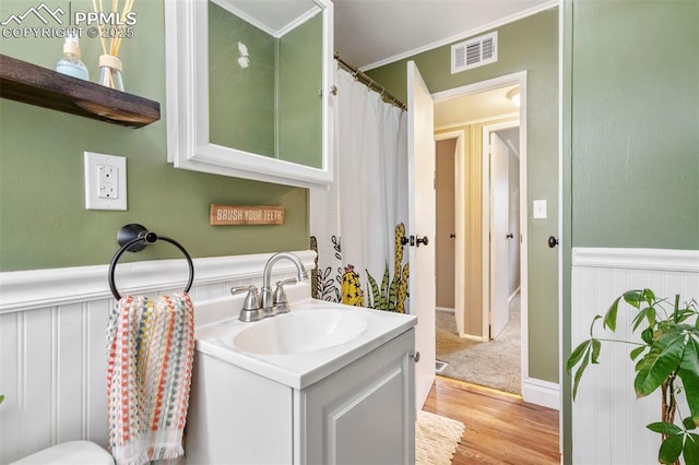 bathroom featuring wood finished floors, ornamental molding, a wainscoted wall, vanity, and visible vents