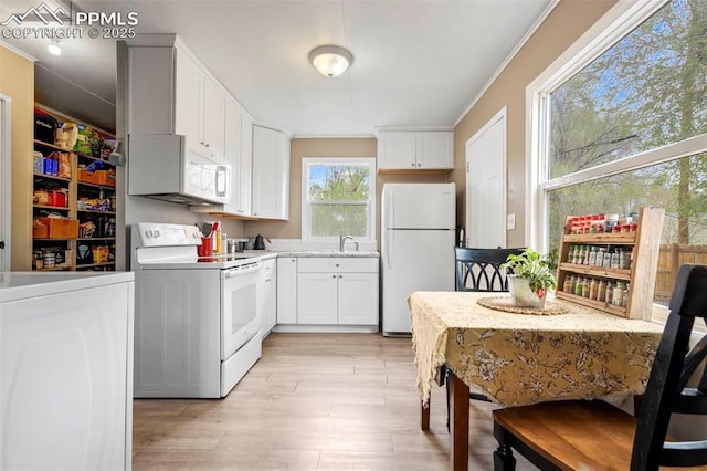 kitchen featuring white cabinets, a sink, light countertops, light wood finished floors, and white appliances