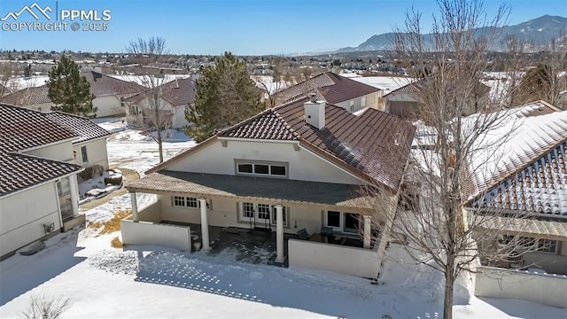 snow covered property with a chimney, a mountain view, and stucco siding