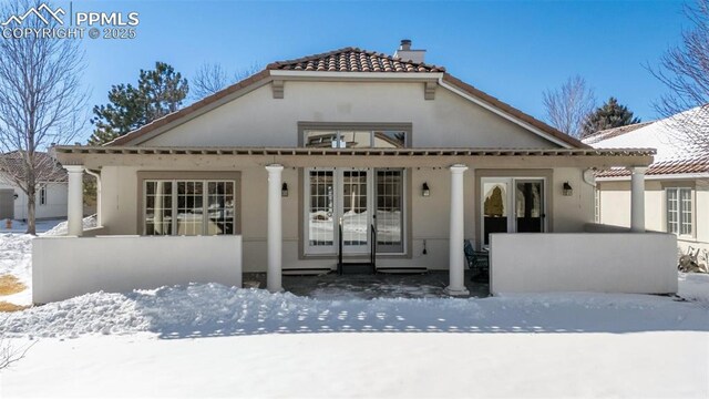 snow covered property with a tiled roof, a chimney, and stucco siding