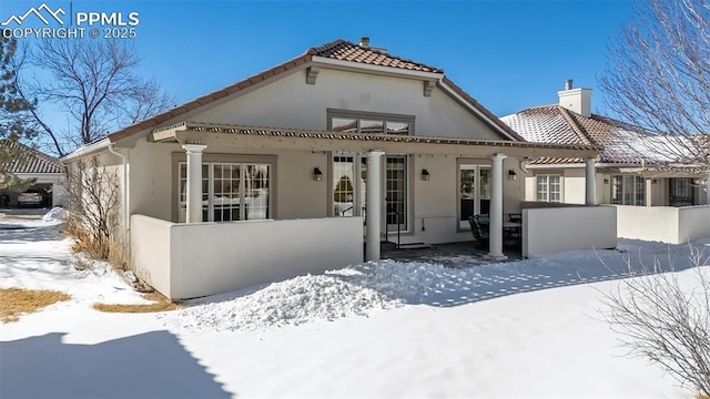snow covered house with a chimney, a tile roof, and stucco siding