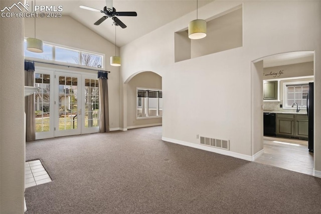 unfurnished living room with high vaulted ceiling, ceiling fan, carpet floors, arched walkways, and visible vents