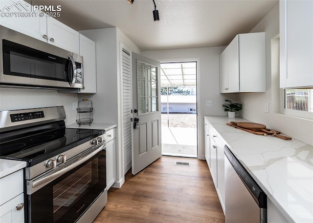 2204 Bonfoy Ave, Colorado Springs, CO 80909 - kitchen with wood finished floors, white cabinetry, stainless steel appliances, and visible vents