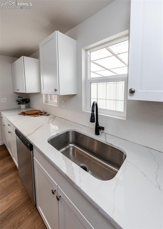 2204 Bonfoy Ave, Colorado Springs, CO 80909 - kitchen with dishwasher, a sink, white cabinetry, and light stone counters