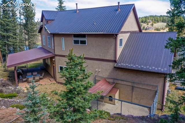 rear view of property featuring fence, a patio, stucco siding, and metal roof