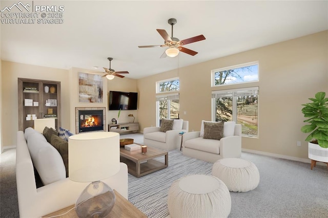 living area featuring a fireplace, baseboards, ceiling fan, and carpet