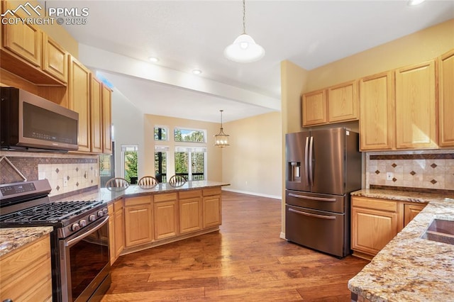 kitchen featuring a peninsula, wood finished floors, light brown cabinetry, appliances with stainless steel finishes, and hanging light fixtures