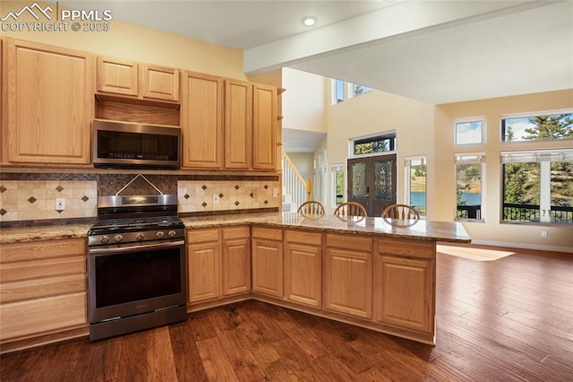kitchen with a peninsula, light brown cabinets, beamed ceiling, appliances with stainless steel finishes, and backsplash