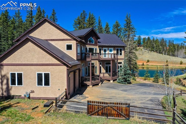 rear view of house with metal roof, a deck with water view, a gate, fence private yard, and stucco siding