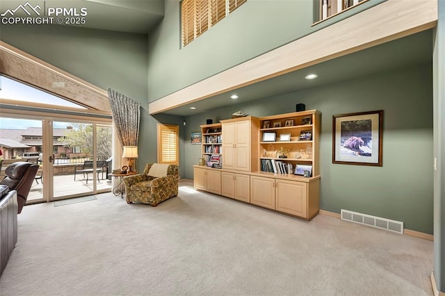 living area with baseboards, visible vents, light carpet, and a towering ceiling