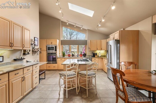 kitchen featuring track lighting, a skylight, light brown cabinetry, stainless steel appliances, and a kitchen island